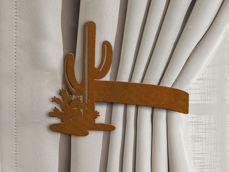 May include: Brown metal cactus curtain tieback. The tieback is shaped like a cactus with a long stem and multiple arms. The cactus is attached to a brown leather strap.
