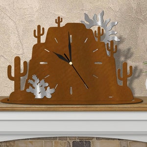 May include: A rusty brown metal clock with a desert scene. The clock features a mountain, cacti, and a sun. The clock is on a wooden shelf.