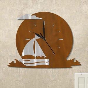 May include: A metal wall clock featuring a sailboat design. The clock has a brown circular background with a silver sailboat and cloud. The clock hands are black. The clock is mounted on a textured beige wall.