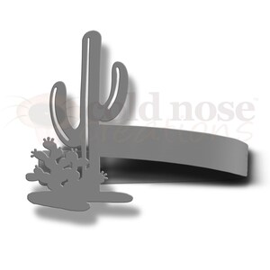 May include: A gray metal wall decor featuring a silhouette of a cactus with a smaller cactus at the base. The decor is shaped like a long, thin rectangle with rounded edges.