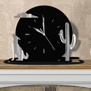 May include: A black metal clock with a silver wolf howling at the moon, a silver cactus, and a silver cloud. The clock is on a wooden shelf.
