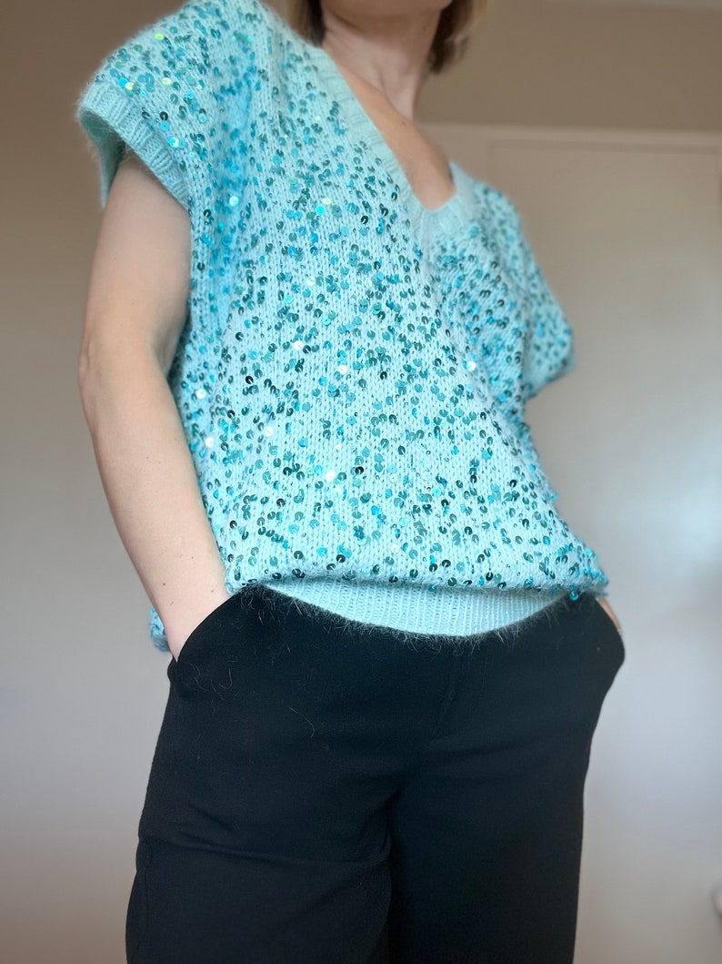 K&ouml;nnte beinhalten: Ein hellblauer Pailettenpullover mit V-Ausschnitt und kurzen &Auml;rmeln.
