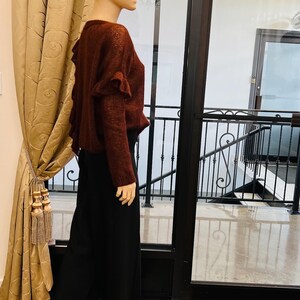 Puede incluir: Un su&eacute;ter marr&oacute;n con detalles de volantes en la espalda. El su&eacute;ter lo lleva un maniqu&iacute; y se combina con pantalones negros de pierna ancha.