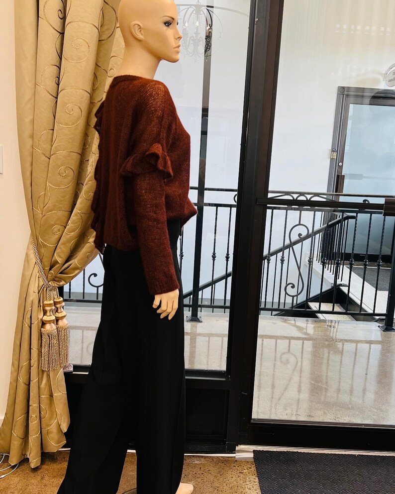 Puede incluir: Un su&eacute;ter marr&oacute;n con detalles de volantes en la espalda. El su&eacute;ter lo lleva un maniqu&iacute; y se combina con pantalones negros de pierna ancha.