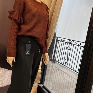 Puede incluir: Un su&eacute;ter de color &oacute;xido con mangas con volantes. El su&eacute;ter est&aacute; hecho de un material suave y peludo. El su&eacute;ter se est&aacute; exhibiendo en un maniqu&iacute; en una tienda.