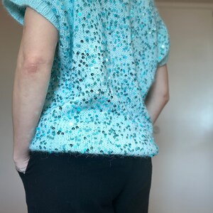 K&ouml;nnte beinhalten: Ein hellblauer Pailettenpullover mit kurzen &Auml;rmeln. Der Pullover ist aus einem weichen, flauschigen Material und hat eine lockere Passform.