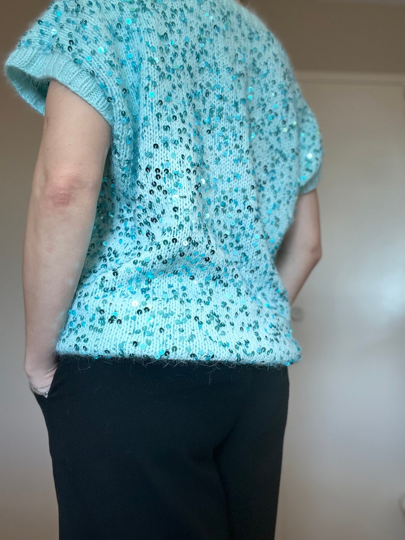 K&ouml;nnte beinhalten: Ein hellblauer Pailettenpullover mit kurzen &Auml;rmeln. Der Pullover ist aus einem weichen, flauschigen Material und hat eine lockere Passform.