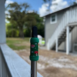 May include: A black and silver vape pen with a green and red mushroom patterned sleeve.