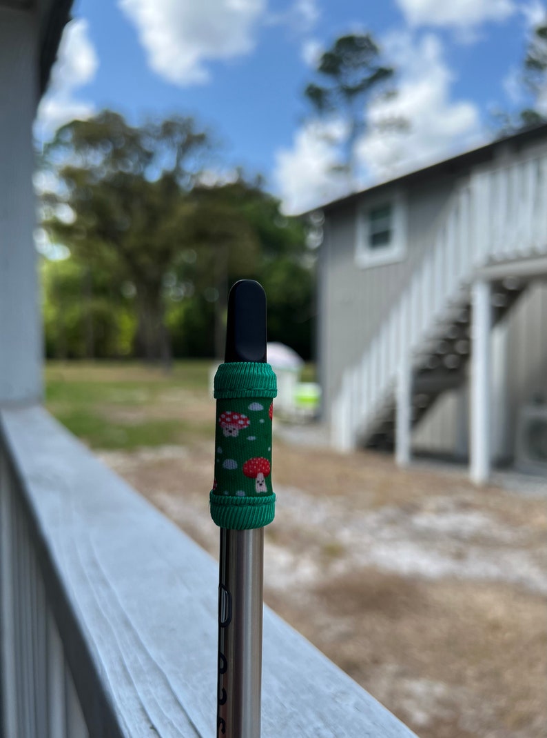 May include: A black and silver vape pen with a green and red mushroom patterned sleeve.