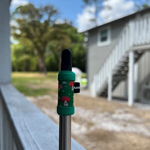 May include: A green and red mushroom-patterned silicone sleeve for a vape pen. The sleeve has a black tip and a black "FLAVOR" tag.