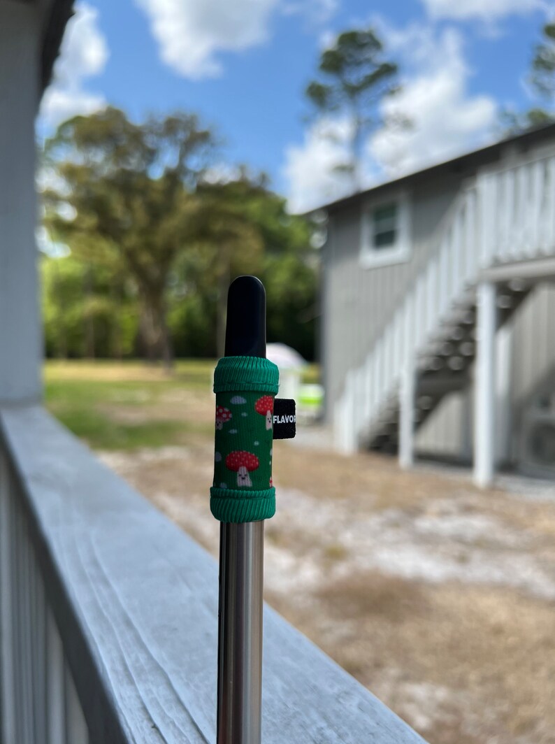 May include: A green and red mushroom-patterned silicone sleeve for a vape pen. The sleeve has a black tip and a black "FLAVOR" tag.
