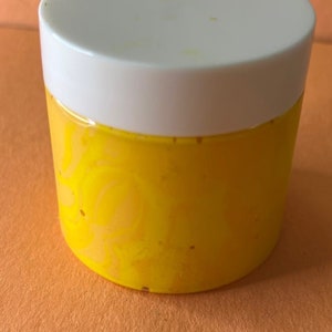 May include: A yellow jar with a white lid filled with a yellow substance. The jar has a swirl pattern.