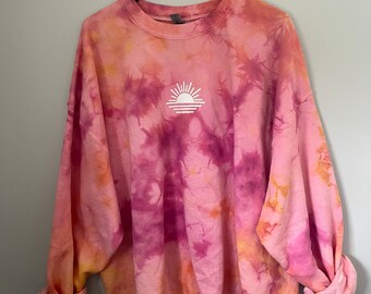 May include: A pink, orange, and purple tie-dye sweatshirt with a white sun graphic on the front.