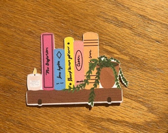 May include: A wooden shelf with a candle, a potted plant, and five colorful books with titles including "The Boy, the Mole, the Fox and the Horse" and "The Alchemist".