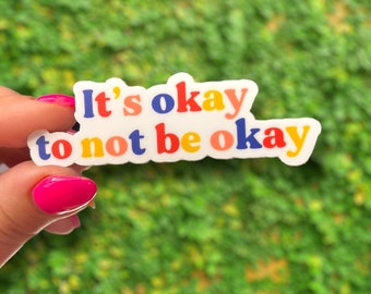 May include: A white sticker with the text "It's okay to not be okay" in colorful letters. The letters are in shades of blue, yellow, red, and orange.