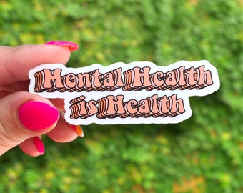 May include: A white sticker with the text "Mental Health is Health" in pink and orange letters with a retro, layered font style.