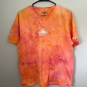 May include: Orange and pink tie-dye t-shirt with a white sun graphic and the text "Emily Bay Designs" and "L" on the front.