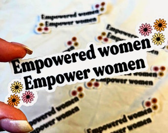 May include: A white sticker with the text "Empowered women Empower women" in black lettering. The sticker has three small yellow, orange, and pink flowers on the bottom left corner.