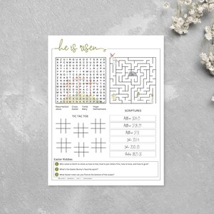 K&ouml;nnte beinhalten: Ein wei&szlig;es Oster-Aktivit&auml;tsblatt mit einem Wortsuchr&auml;tsel, einem Labyrinth, Tic-Tac-Toe, R&auml;tseln und Bibelstellen. Der Satz "he is risen" ist in goldener Schrift geschrieben. Das Blatt ist mit einfachen Strichzeichnungen verziert.