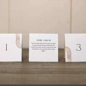 May include: Three white cards with gold accents and black numbers. The middle card has the text "LUKE 1:30-31" and a Bible verse about the birth of Jesus. The cards are numbered 1, 2, and 3.