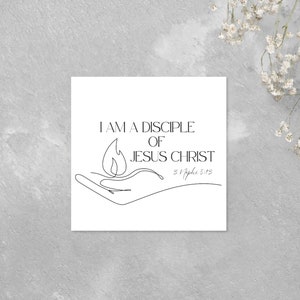 May include: A white card with black text that reads "I am a disciple of Jesus Christ" with a flame in a hand drawn in black line art. The scripture reference "1. Apostle 5:18" is written below the text.