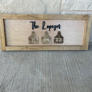 May include: A wooden sign with the text "The Lopezes" and three wooden tags with the numbers "11", "04", and "23" hanging from it.