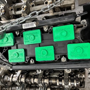 May include: An engine block featuring green Pentastar 3.6 covers. The engine is partially dismantled, revealing chains, gears, and a metal hook. The covers display the text "PENTASTAR 3.6" and "RDE".
