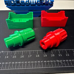 Op de afbeelding: Een verzameling 3D-geprinte onderdelen in groen en rood. De groene onderdelen omvatten een rechthoekige container en een cilindrisch onderdeel met de tekst "Diff Case". De rode onderdelen omvatten een vergelijkbare container en een cilindrisch onderdeel. Een blauw bord met de tekst "ADLadworkz" op de achtergrond.