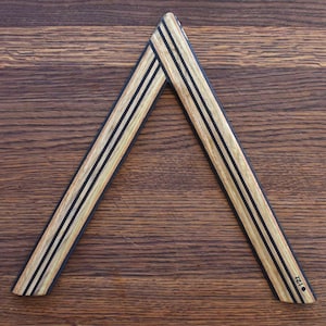 May include: A wooden triangle with black stripes, the triangle is made of wood veneer and has a black dot on the bottom point.