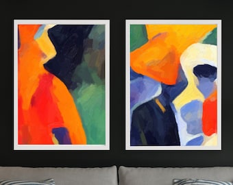 May include: Two abstract art prints in white frames. The artwork features bold shapes and colors, including orange, red, blue, and green. The prints are displayed above a gray sofa with striped pillows, a teal throw, and a white coffee table.