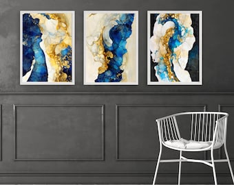 Puede incluir: Tres impresiones de arte abstracto con patrones de remolinos azules, dorados y blancos. Las impresiones están enmarcadas en blanco y están colgadas en una pared gris oscuro.