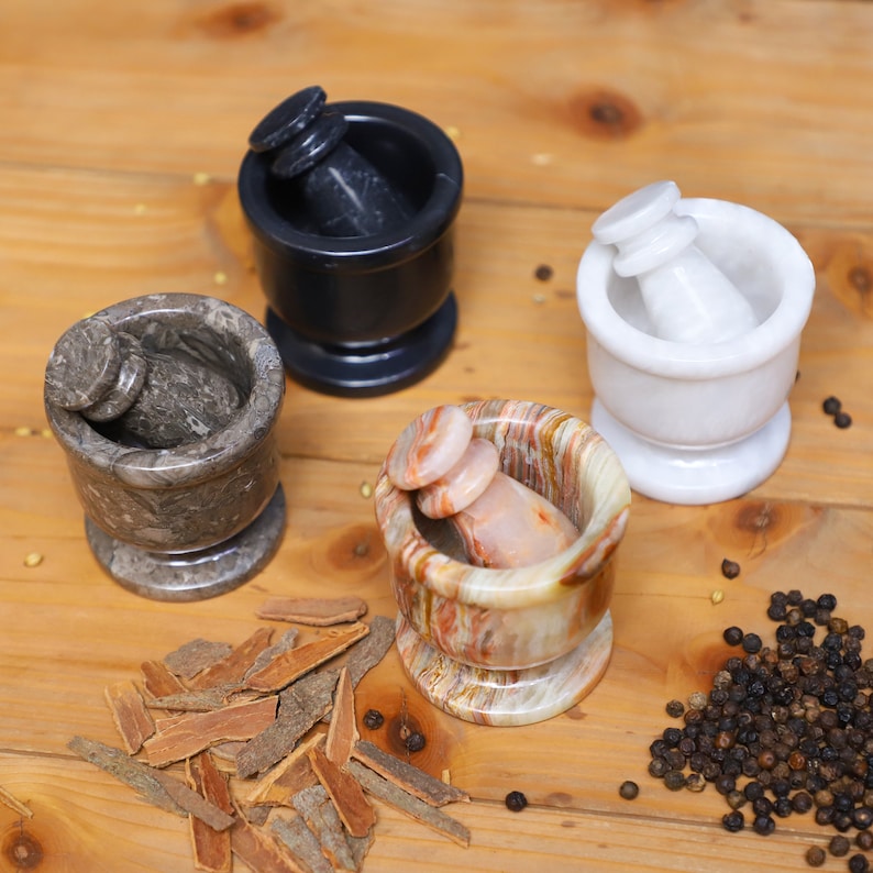 Puede incluir: Cuatro juegos de mortero y maja de piedra en m&aacute;rmol negro, gris, blanco y multicolor. Los morteros son cil&iacute;ndricos con base redondeada, y las majas tienen un mango redondeado. Palitos de canela y granos de pimienta esparcidos.