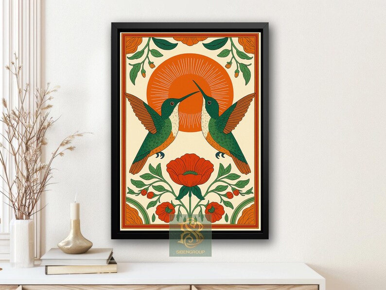 May include: Framed art print featuring two green and orange hummingbirds touching beaks, set against a cream background with an orange sunburst. The artwork includes red flowers and green foliage, all within an orange border.