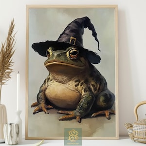 May include: A framed print depicting a frog wearing a black witch's hat with a gold buckle. The frog is rendered in green and brown tones, and the artwork has a vintage, painterly style. The print is in a wooden frame.