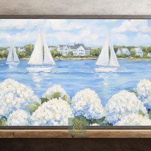 May include: A framed painting depicts sailboats on a blue sea, with white houses in the background under a cloudy sky. White hydrangeas are in the foreground. The artwork is in a gray frame.
