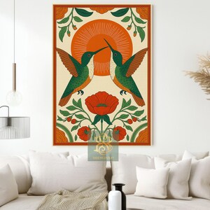 May include: A framed art print featuring two hummingbirds facing each other, with a red flower and sun design. The birds are green and orange, set against a cream background with an orange border. The artwork is displayed on a wall above a sofa.