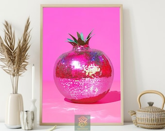 May include: A framed print featuring a pink disco ball pomegranate with green leaves against a bright pink background. The artwork is displayed on a white surface with decorative items, including a vase with dried plants and a teapot.