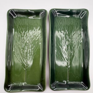 May include: Two rectangular ceramic serving trays in a deep forest green glaze. Each tray features a raised, embossed wheat stalk design centered on the base. The edges of the trays are slightly curved and raised, creating a smooth, glossy finish.