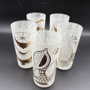 May include: Set of five vintage highball glasses with gold fruit designs on a speckled white background. Each glass features a different fruit illustration, including a lemon, pineapple, and other citrus fruits. The glasses are cylindrical and have a mid-century modern aesthetic.