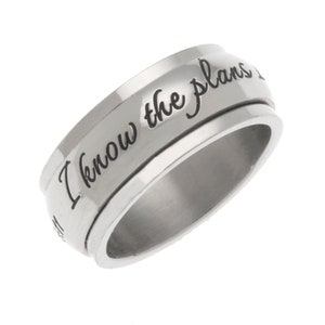 May include: A silver spinning ring with the inscription "I know the plans I have for you" in black lettering.