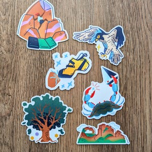 May include: Set of seven colorful stickers featuring outdoor adventure themes. The stickers include a climber on a rock face, a falcon in flight, a pair of climbing shoes, a crab with a star, a tree, and a mountain range.