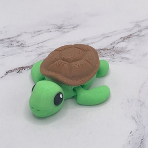 May include: A small, green plastic turtle toy with a brown shell. The turtle has a cute face with black eyes and a slight smile.