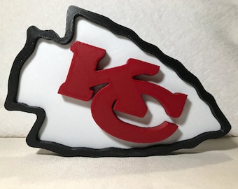 May include: A red and black 3D printed arrowhead with the letters "KC" inside. The arrowhead is a popular symbol for the Kansas City Chiefs.