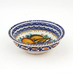 May include: A ceramic bowl with a white interior and a blue and white patterned rim. The bowl features a hand-painted design of fruit in shades of orange, yellow, and blue. The bowl is approximately 8 inches in diameter.