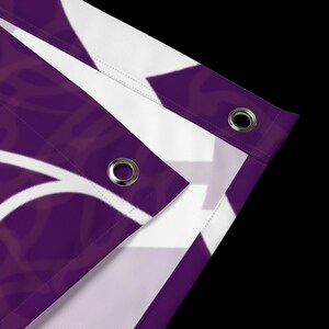 May include: Close-up of a purple fabric banner with white eyelets. The banner has a white design on it.
