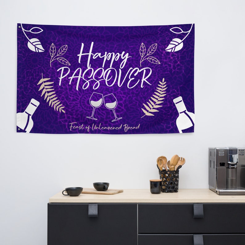 May include: Purple banner with the text "Happy Passover Feast of Unleavened Bread" in white lettering. The banner also features two wine glasses clinking, a bottle of wine, and leafy branches.