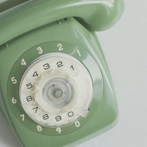 Op de afbeelding: Een vintage groene draaischijftelefoon met een wit wijzerplaat en zwarte cijfers. De telefoon heeft een groene hoorn.