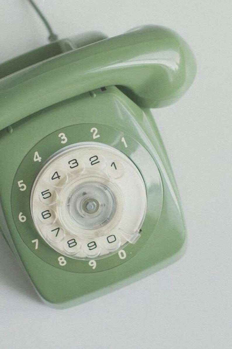 Op de afbeelding: Een vintage groene draaischijftelefoon met een wit wijzerplaat en zwarte cijfers. De telefoon heeft een groene hoorn.
