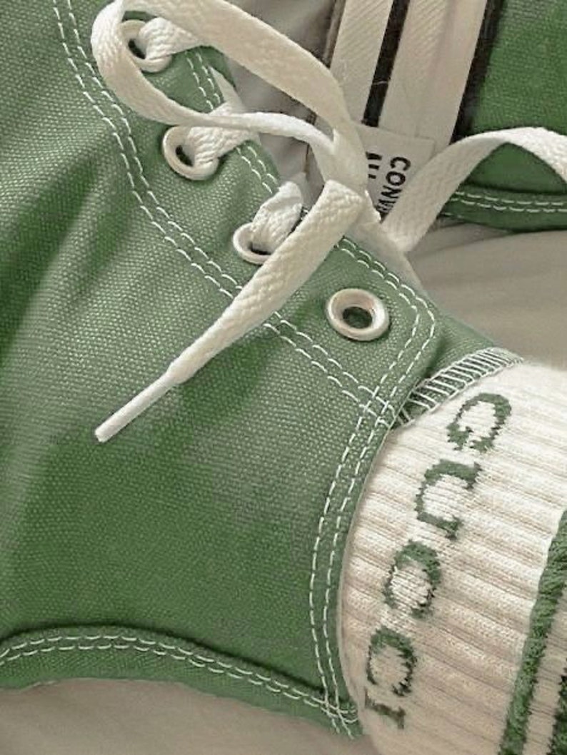 Op de afbeelding: Close-up van een paar groene canvas sneakers met witte veters en een witte sok met het woord "Gucci" erop geborduurd.