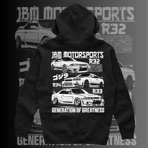 May include: Black hooded sweatshirt with a white graphic print of three Nissan Skyline R32, R33, and R34 cars. The text "JBM MOTORSPORTS" and "GENERATION OF GREATNESS" is printed on the sweatshirt.